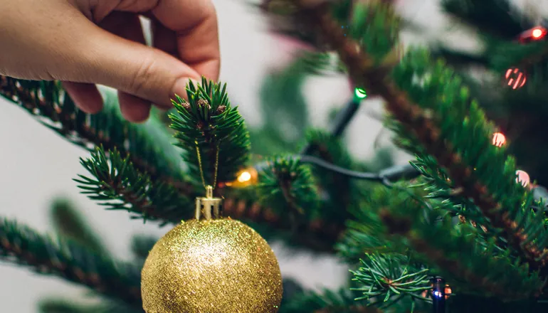 Main accrochant une boule dorée sur un sapin