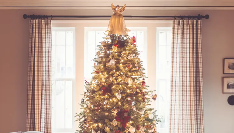 Grand sapin décoré devant une fenêtre de salon