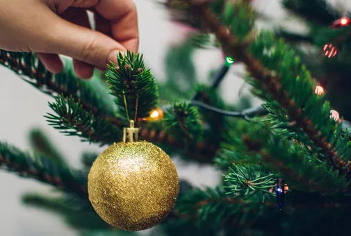 Main accrochant une boule dorée aux branches d'un sapin