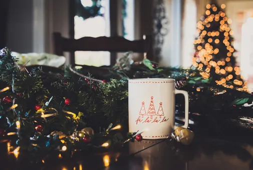 Tasse de Noël sur une table, avec un sapin illuminé en arrière-plan
